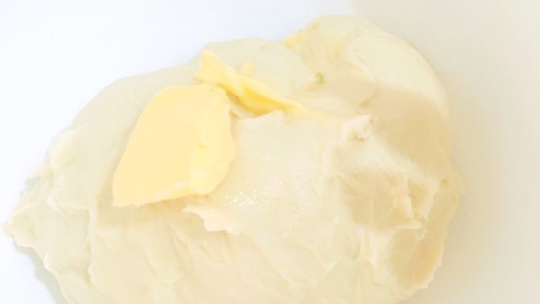 长得像花环的日式炼乳手撕面包,取出面团,放入搅拌盆内,倒入剩下的软化了的2.5g黄油,手揉5分钟。