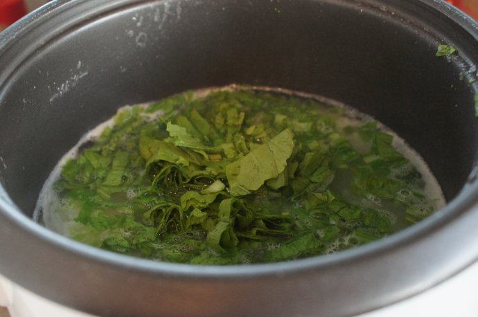 电饭锅芥菜肉粥,粥煮好了，加入芥菜。搅拌均匀，大致把芥菜煮软