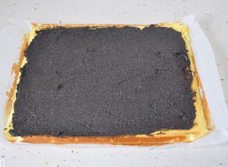 【红枣黑芝麻蛋糕卷】,取出不要揭掉烘焙纸的放置,自然降温后均匀抹平一层黑芝麻馅。