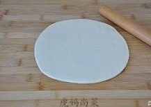 【培根披萨】,将面团分成两个相同的剂子,取其中一个,擀成圆形薄片状。