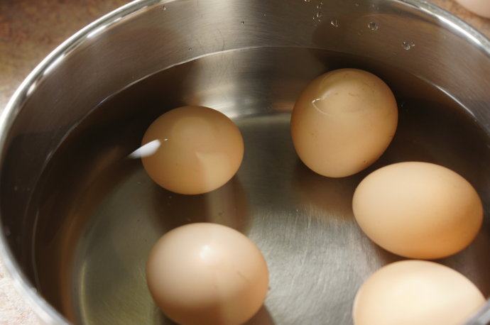 跟孩子做惊悚又美味的蜘蛛蛋——Spider Eggs ,把鸡蛋放入锅中,加冷水没过鸡蛋,中小火将鸡蛋煮全熟。