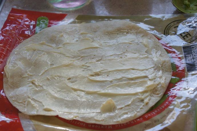 健康快手的素食午餐——墨西哥素卷 ,把软化的奶油奶酪涂抹在玉米圆饼上。