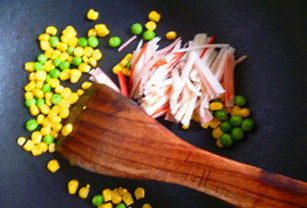 海鲜菠萝炒饭,利用锅中剩余的油翻炒玉米和青豆，略炒软即可加入蟹肉棒略翻炒几下。