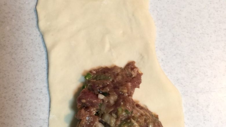 香煎牛肉饼,用擀面棒把面团擀成长条,我分成的60克一个的面团,然后放入馅儿料,卷起来,竖着放再用手轻轻压