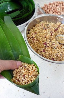 香浓里脊肉粽,将苇叶码齐后将宽头的一端窝成一个三角漏斗状,依次放入拌好的糯米、肉,中间放几粒花生米。