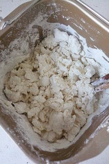 【葱油饼】,将滚水倒入加了盐的面粉中,迅速的用筷子扮成面絮,尽量的烫熟一大部分的面。