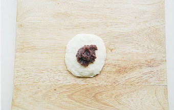 【杏仁豆沙面包】,取一个面团摁扁,中间放入<a style='color:red;display:inline-block;' href='/shicai/ 475'>红豆沙</a>;