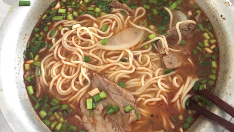 简易兰州清汤牛肉面,冲面。准备一个或几个大碗,把煮好的面捞到碗里,放入切好的牛肉、蒜苗、香菜、萝卜,用大勺将牛肉汤浇入,最后浇辣子油。OK。