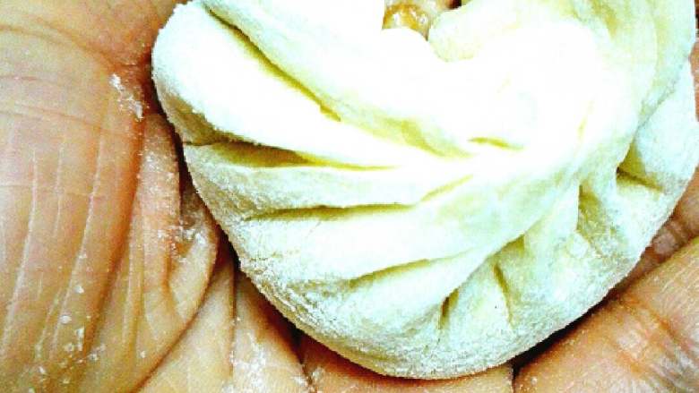 手工肉包子,拇指支住面皮，食指开始均匀地打摺收皮，收好按以下