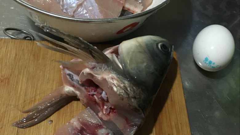 妈妈厨味—回锅鱼,4.鱼头鱼尾留下备用,看见那白瓷盆了没,把刚切的鱼片抹上盐放入盐和料酒腌制片刻,再放鸡蛋清和淀粉腌制。