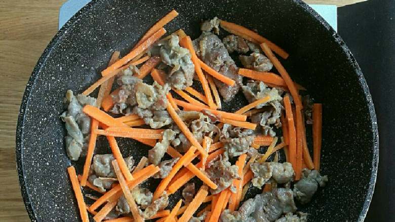 牛肉泡菜糙米饭,锅中高火加热,倒入少许油,倒入肥牛肉片炒至半熟,然后倒入胡萝卜丝一分钟。