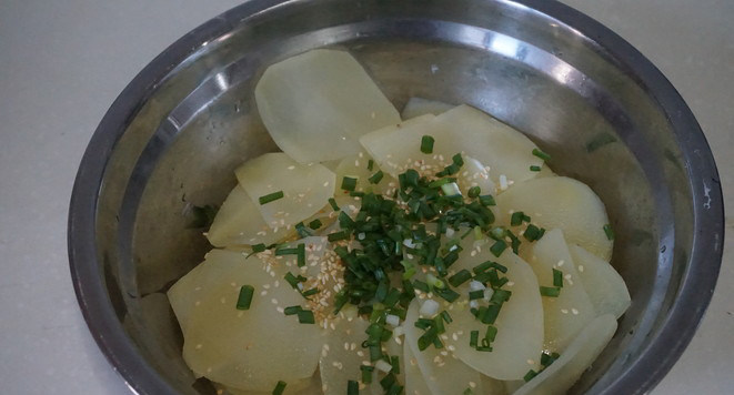 响油土豆片,焯好的土豆捞起盆内,加入白芝麻和葱花。