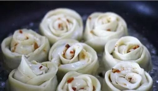 玫瑰花煎饺,煎到底部微微有点黄时加入少许开水,盖上锅盖焖,焖干水汽接着加入少许水再焖干,再加入少许水再焖干就熟了,一共加三次水。煎的时候在表面淋入调味汁,出锅前撒上熟芝麻。