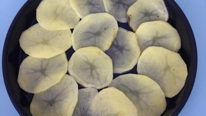 火腿芝士烤土豆片,披萨盘涂一层黄油或食用油,将土豆片码放入披萨盘中。
