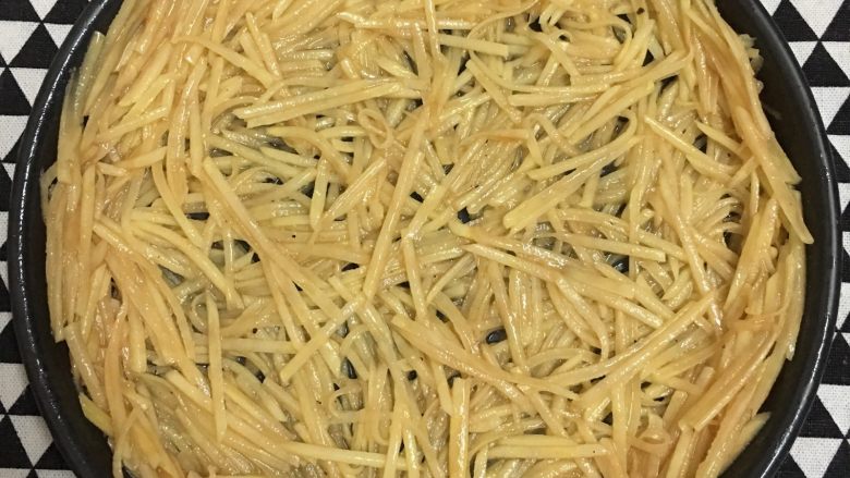 土豆丝培根披萨,披萨盘抹一层黄油或食用油,将拌好的土豆丝铺入披萨盘中。