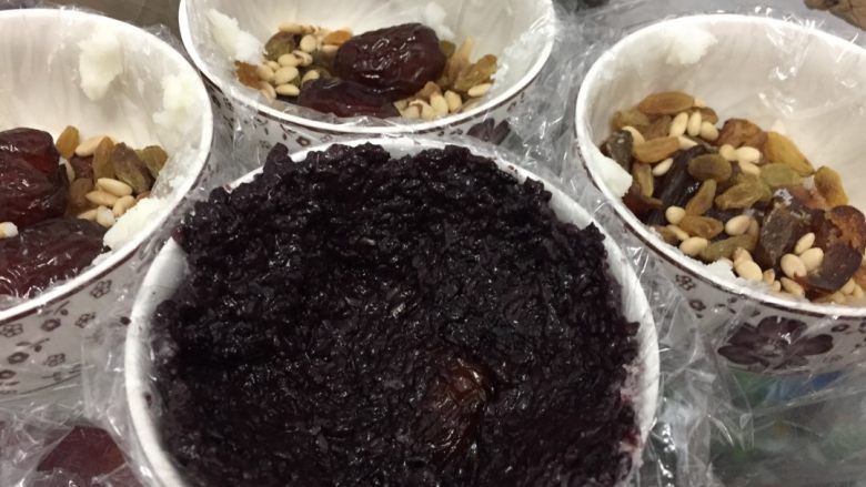 黑米八宝饭,在铺好干果的碗里加入搅拌好的黑米糯米,用勺子将其铺匀,留一个凹槽。