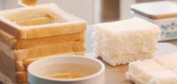 蜂蜜厚士多,面包片置于底部,然后将挖空的面包框四角粘花生酱,逐一垒起,搭成一座小小的城堡。