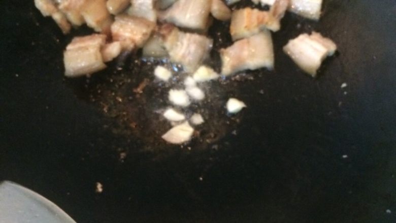 豆角干焖五花肉,五花肉放锅旁，下蒜粒爆香，之后跟五花肉一起翻炒几下