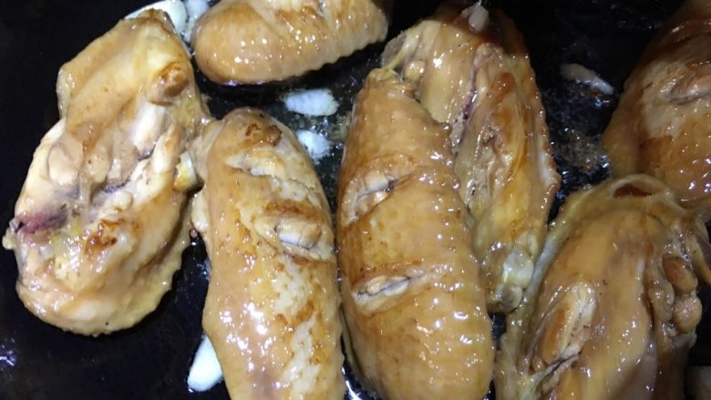 咖喱鸡翅焖饭,煎好的鸡翅盛出,锅内放入蒜片炝锅,再倒入鸡翅翻炒,加入适量酱油。