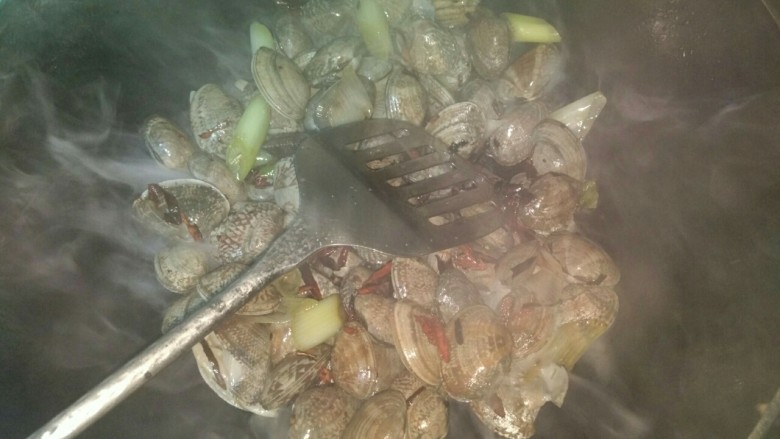 爆香花蛤,锅中热油,先放入部分葱段和辣椒爆香,再倒入花蛤,放少许盐,大火翻炒至出汤。再放入剩余的葱段和辣椒翻炒一下后盖上盖。