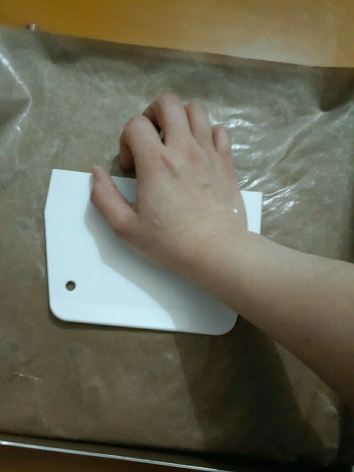 抹茶白巧牛轧糖,然后把油布另外那边盖上,用刮板贴在糖上面,滑行挤压平整