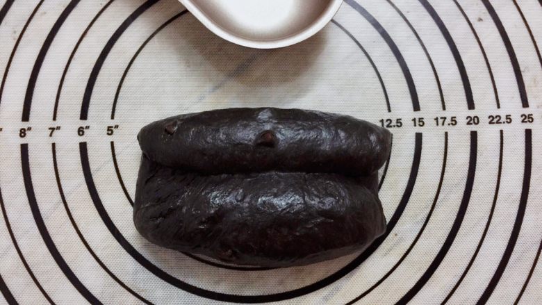 黑可可热狗包,取一小份面团,擀成椭圆形,两边向中间卷起,收口捏紧,搓成橄榄形