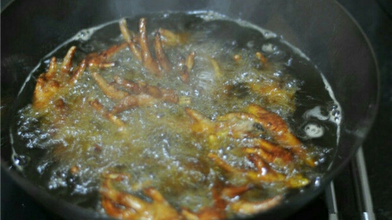 虎皮鸡爪,摇晃锅子,让鸡爪均匀泡在油里,待锅不再爆油时,揭开盖子,炸至皮紧发硬出纹