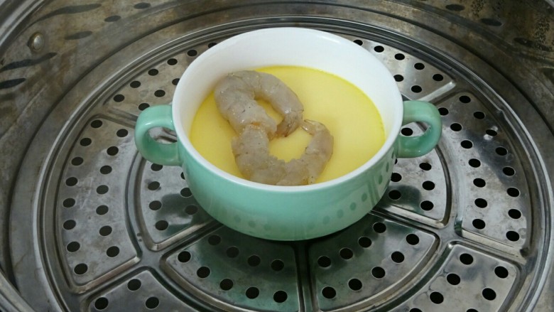虾仁蒸蛋羹,15分钟以后,蛋液已经基本凝固了,打开保鲜膜,把虾仁放在上面,摆成一个心形,盖上保鲜膜,继续蒸五分钟,虾仁熟透即可。