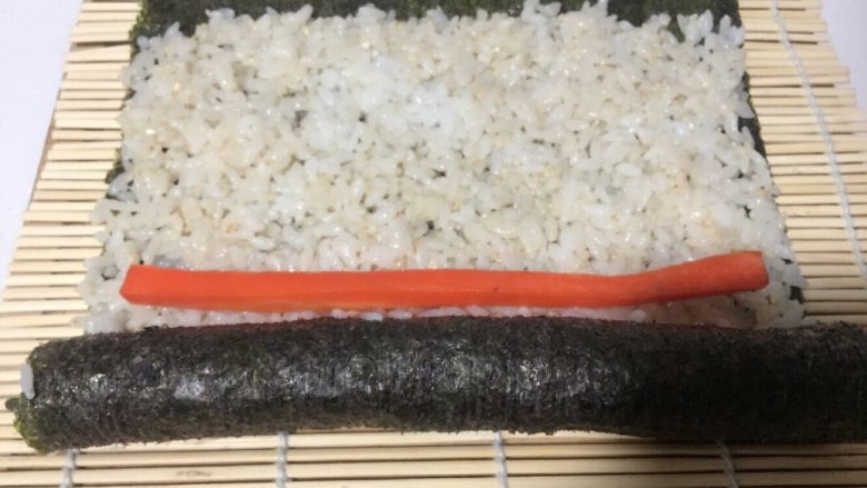 酱香味秋葵寿司(纯素版),打开竹席,再放一根胡萝卜条,然后再用竹席继续卷