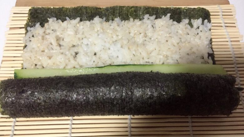 酱香味秋葵寿司(纯素版),打开竹席放一根黄瓜条,用竹席继续卷