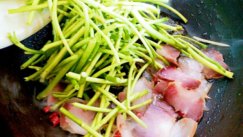 泥蒿炒腊肉,辣椒段和姜丝炒好后,再把泥蒿倒入锅内。