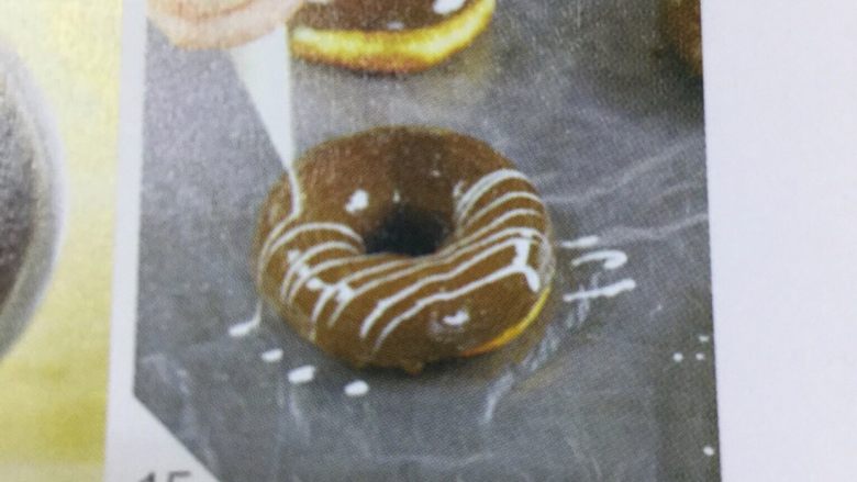 巧克力甜甜圈,6 将黑、 白巧克力切小块，分别隔水加至融化，将甜甜圈的一面用勺子淋上巧克力，涂抹均匀，放在铺有塑料布的烤盘上。用裱花袋将白巧克力挤在涂有黑巧克力的一面进行装饰， 成丝状即可。