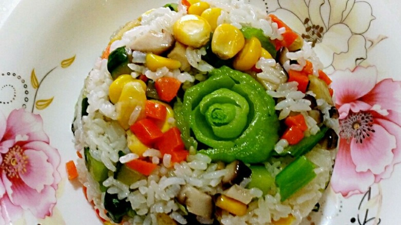 春暖花开缤纷拌饭,上海青根部用隔水法稍微加热后,取一个食用碗把花倒扣在碗的中间,勺入拌好的饭用饭勺压平压紧,倒扣到盘中即可。