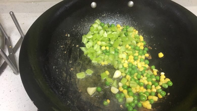 清炒三色扇贝柱,倒入玉米粒、小豌豆和青椒粒,翻炒2分钟,锅铲晃动起来,以免粘锅