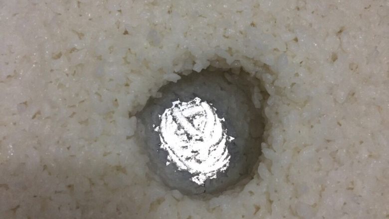家庭简易版自制酒酿,第四步,蒸熟后冷却至不烫手时加入事先准备好的凉白开搅拌均匀。然后加入<a style='color:red;display:inline-block;' href='/shicai/ 9700'>酒曲</a>搅拌均匀。我用筷子搅拌并用勺子压成图片形状
