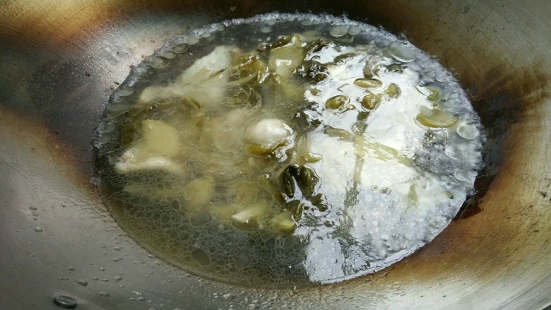 酸菜鱼,待鱼骨六成熟时加入酸菜,翻动几下,加入水,白醋