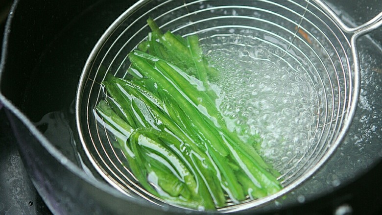 夏日小菜凉拌土豆丝,青椒丝放在沥勺内,放在开水里过一下水立刻捞起。