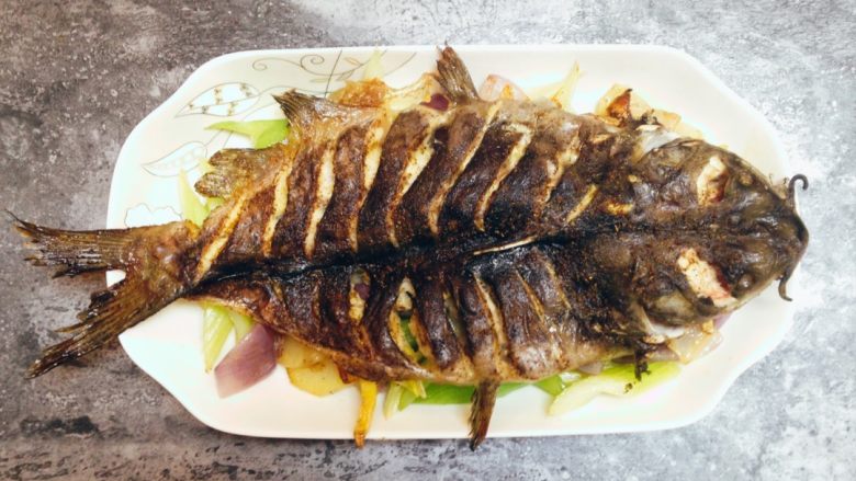香辣烤鱼,将烤好的鱼移入鱼盘,鱼背向上铺放在炒好的菜上面。