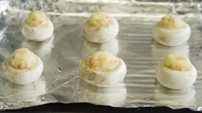 香酥烤蘑菇,用小勺把土豆泥塞到蘑菇里,不用塞很紧,但是尽量多堆一些,还可以在上面裹上一些芝士碎,放到铺有锡纸的烤盘上(可以先在要放蘑菇的位置刷 一点点油