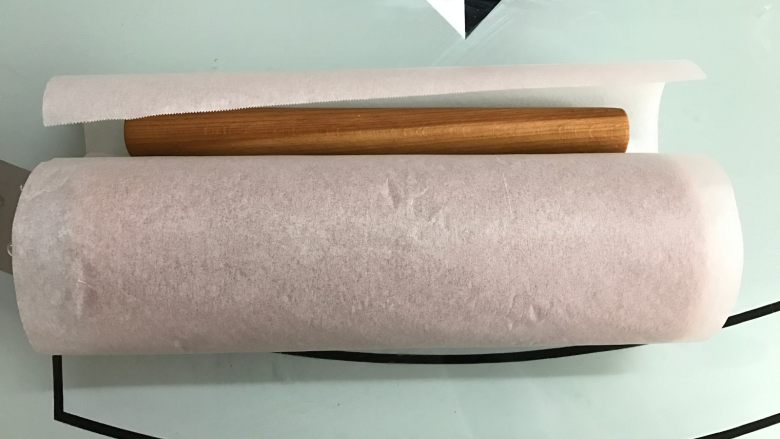 黑米戚风蛋糕卷,借助擀面杖将蛋糕卷起来,用油纸卷起来放入冰箱冷藏定形30分钟以上。