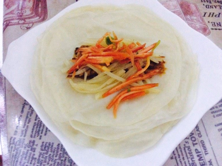 蒸多层煎饼,先抹上酱,夹上菜,卷好。