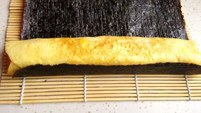 紫菜蛋包饭,将做好的鸡蛋卷取出,放在<a style='color:red;display:inline-block;' href='/shicai/ 54263'>烤紫菜</a>片上,用寿司卷帘辅助,小心卷起