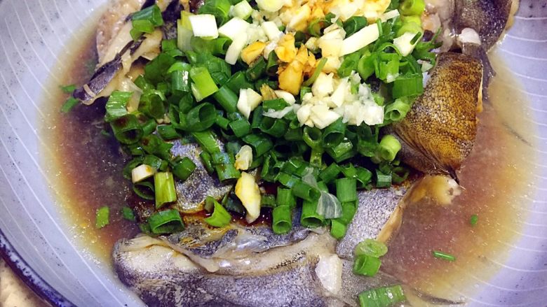 葱油鸦片鱼头,鱼从蒸锅端出,去掉姜片,放葱花、蒜泥,倒入适量的美味鲜酱油;