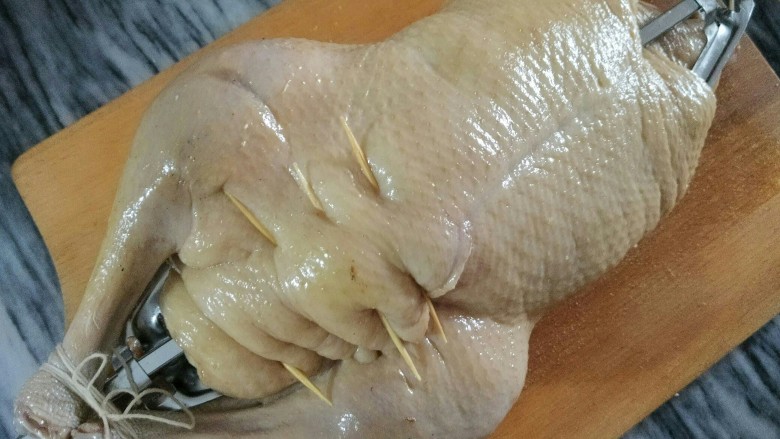 蜜汁烤全鸭,用浸湿的棉线绑好鸭腿,烧烤叉穿好,拧紧