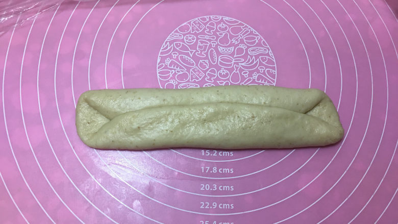 燕麦辫子花环汉堡面包,醒发完毕后,取一个面团擀开,翻面过来后横放面团,将上下对折。