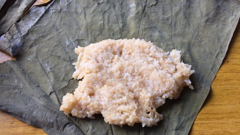 荷叶糯米鸡,在靠近荷叶尖角处,放上一勺米饭,稍稍压平