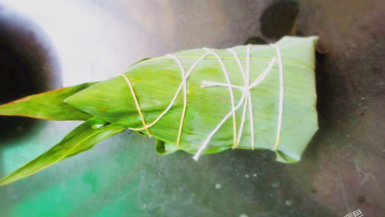 五花肉粽,用左手手虎口处把住粽子底部及中间部分,再用多余的粽叶覆盖住糯米,捏紧、缠上绳子,绑好