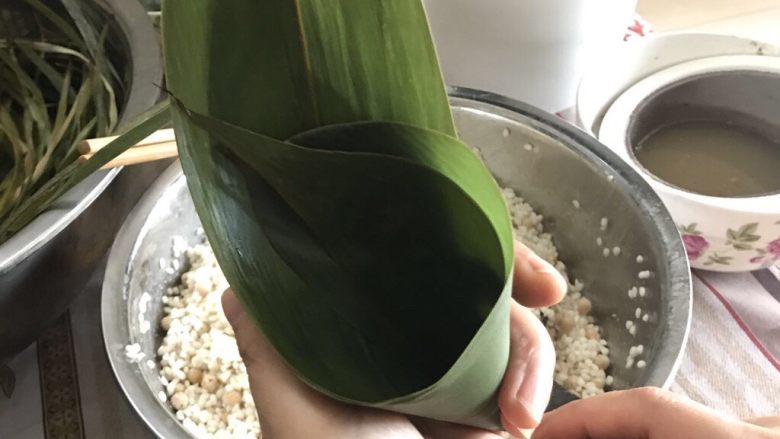 肉粽子,两片叶子卷成图中形状,加入一勺前面拌好的糯米,中间加入一块猪肉,再放入一勺前面拌好的糯米(具体以叶子大小决定)