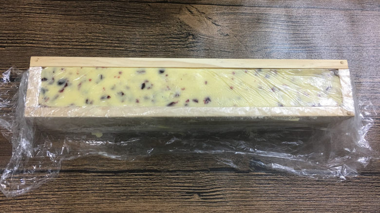 蔓越莓曲奇饼干,分一半放在保鲜膜里,然后放进长方形的蔓越莓模具中压平压实。