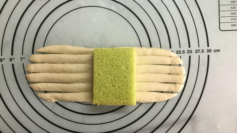 蛋糕夹心面包,取一面团,稍加按扁后擀成长舌形,中间放上切小块的蛋糕。
长舌形两端用刮板切成条。